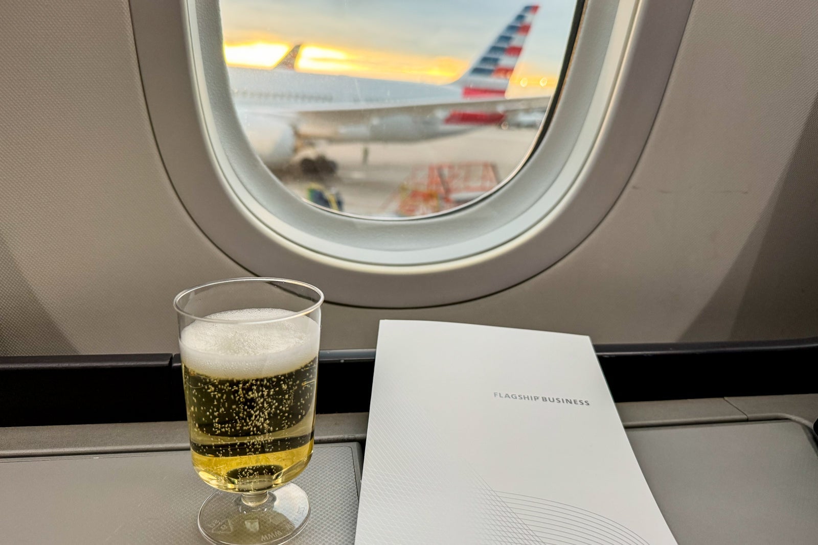 a glass of Champagne sitting on a tray in front of an airplane window