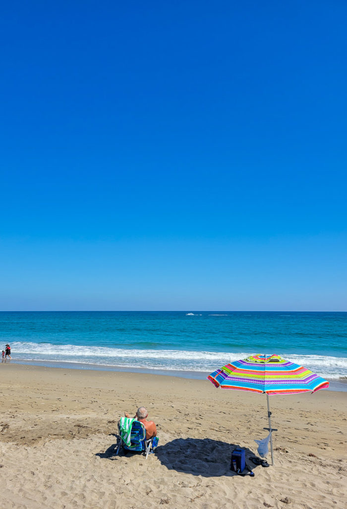 man sitting on chair at the beach next to beach umbrella